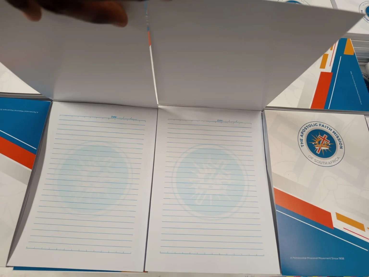 Open branded notepad showing lined writing pages with a light blue watermark