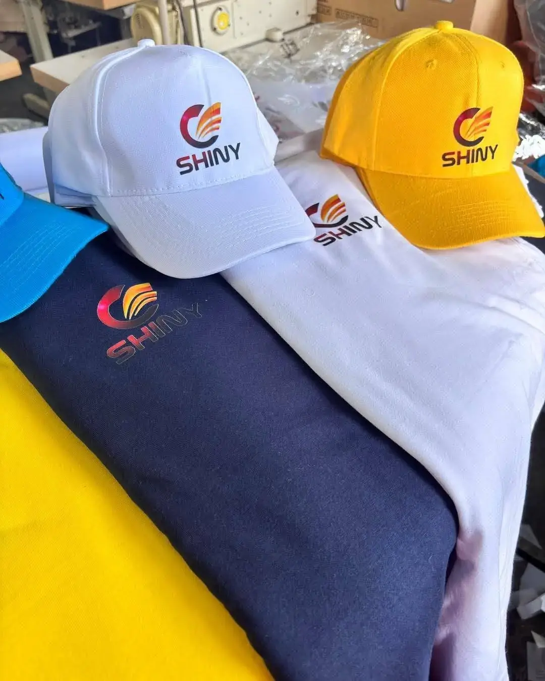 Bulk embroidered caps stacked beside commercial embroidery equipment