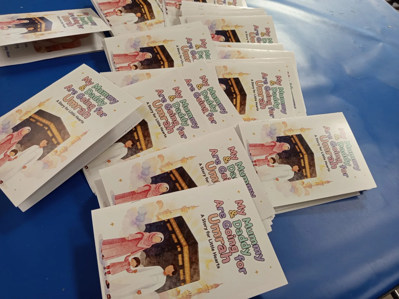 Stacks of finished children’s Umrah booklets arranged after printing and saddle stitching