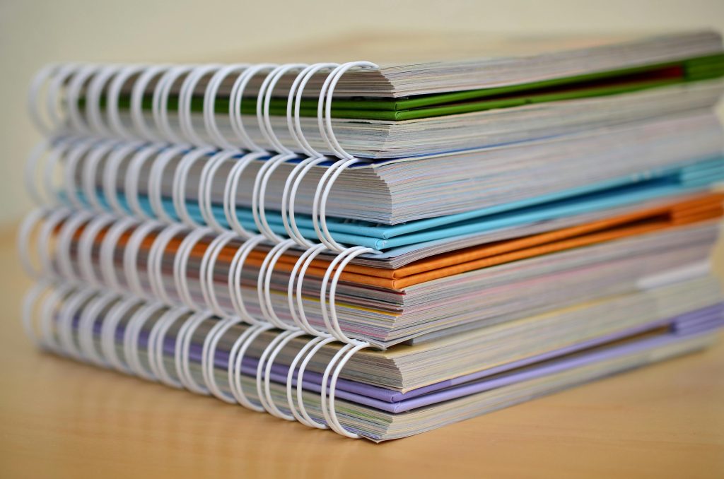 Training Manual Printing Johannesburg A colorful stack of spiral-bound notebooks neatly placed on a wooden desk. Ideal for educational themes.