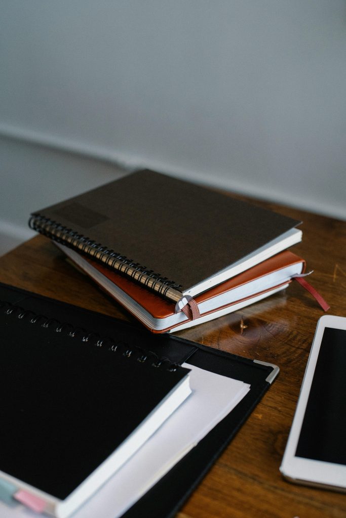 High angle of paper notebooks and modern tablet on wooden table in office