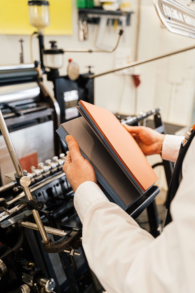 The Complete Guide to Book Printing Johannesburg: From Thesis to Hardcover Person holding papers near a printing press in a workshop setting.